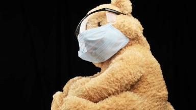 棕色（的）泰迪熊坐在保护塑料眼镜医疗一次性面具概念儿科黑色的背景
